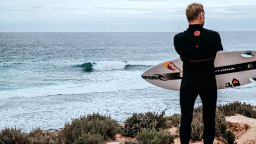 Man standing on a cliff with his surfboard.